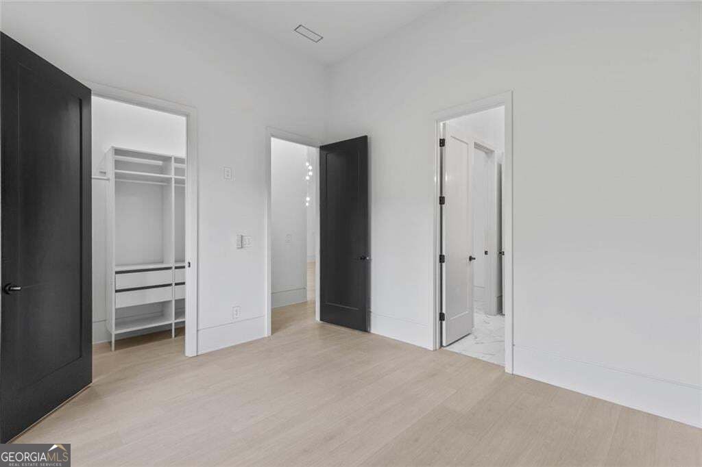 Empty bedroom with light wood flooring, open closet shelving, and dark interior doors.