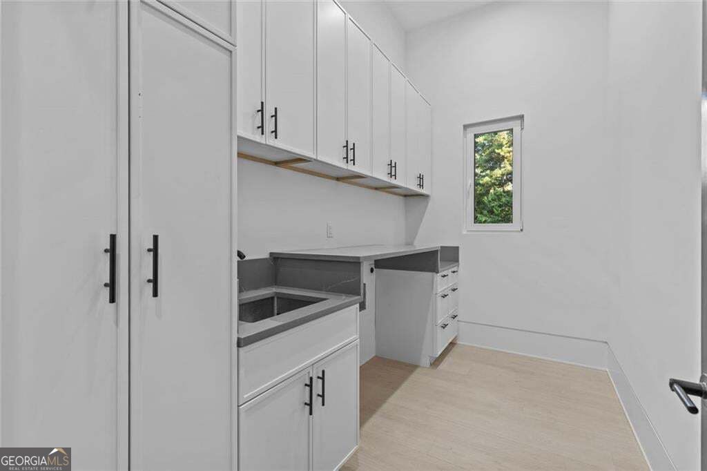 Laundry room with white built-in cabinets, gray countertops, and a narrow window overlooking greenery.