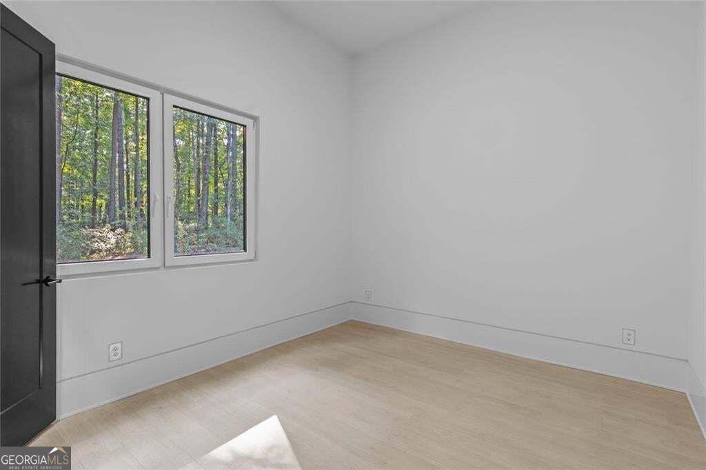 Empty room with pale wood floors and two windows overlooking trees.