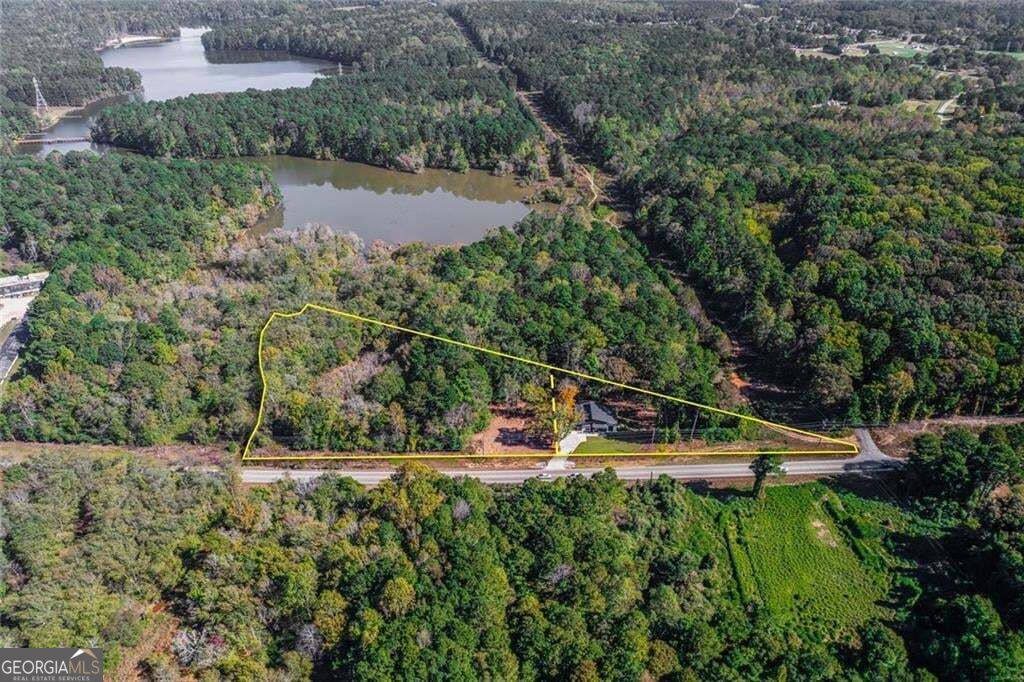 Aerial view of a wooded parcel outlined along a highway, with a small building and water nearby.