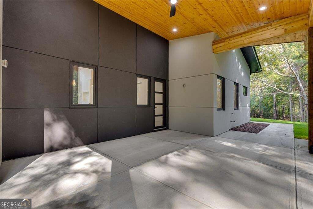 Modern home’s covered entry with dark panel siding, a wood-plank ceiling, and a broad concrete floor.