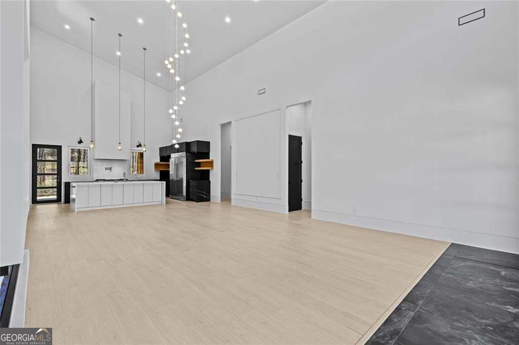 Open-plan kitchen with a white island, black cabinetry, pale floors, and dramatic high ceilings.