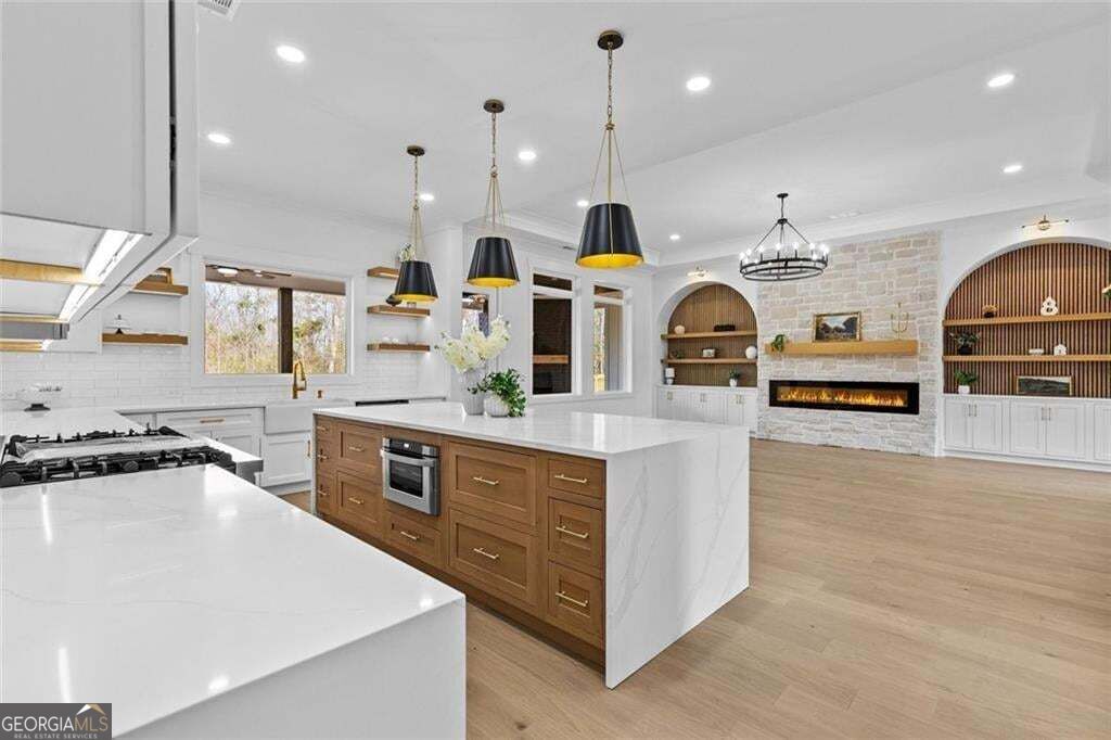 Open kitchen with a large white island, wood cabinetry, and an adjoining stone fireplace.