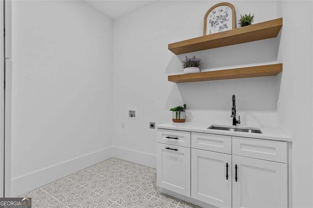 Utility room with white cabinets, a stainless sink, floating wood shelves, and patterned tile flooring.