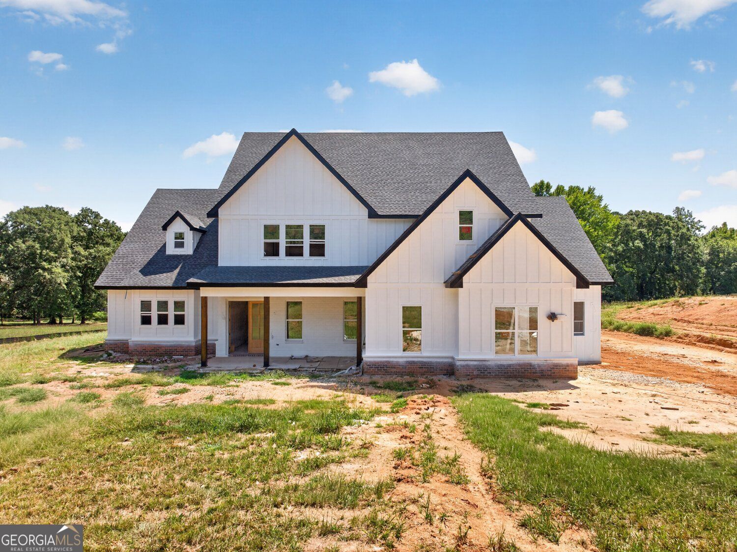 White multi-gabled house under construction, with a dark roof and unfinished red-soil yard.