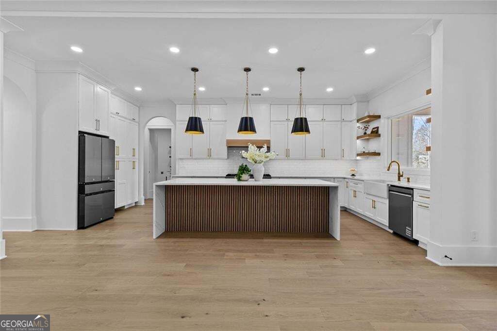 Kitchen with white cabinetry, a wood-front island, three pendant lights, and a sink beneath the window.