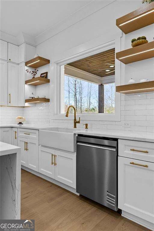 Bright white kitchen with brass fixtures, a farmhouse sink, and a window overlooking leafless trees.