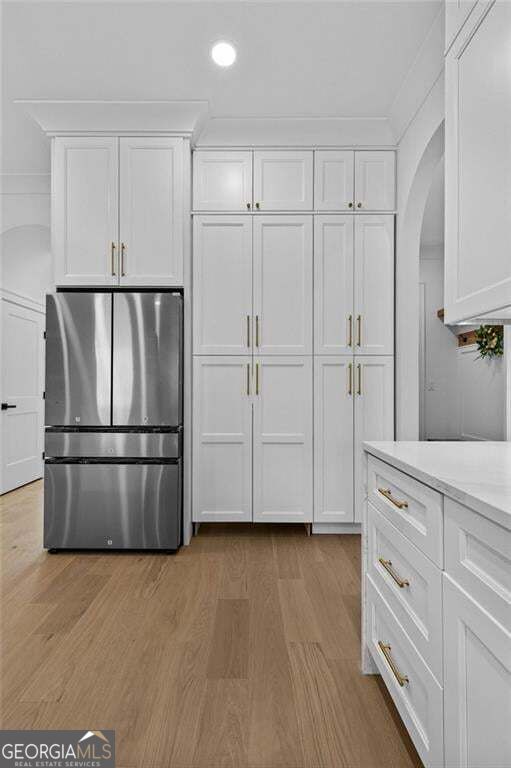 Kitchen with white cabinetry, a stainless-steel refrigerator, and light wood flooring.