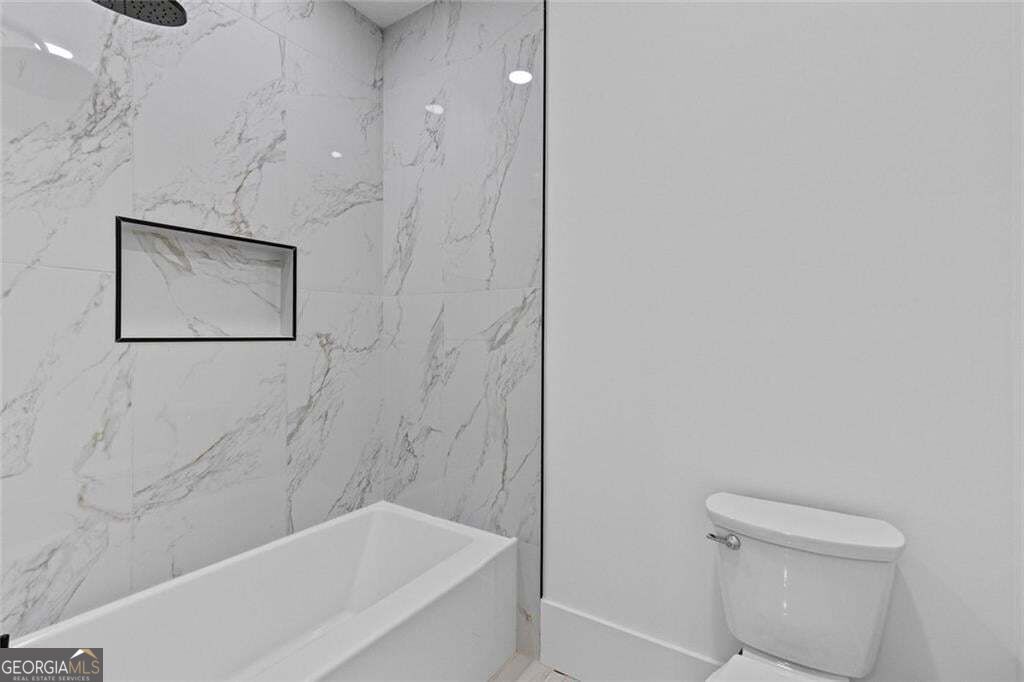 Bathroom with a white bathtub, marble-look shower surround, recessed niche, and toilet.