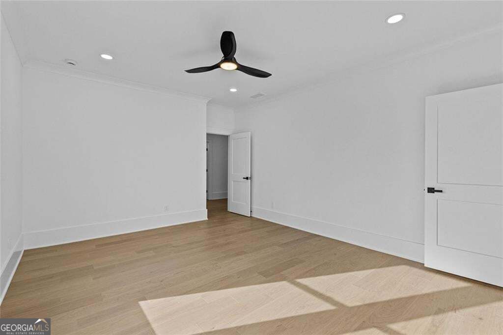 Empty room with light wood floors, white walls, a black ceiling fan, and sunlight across the floor.