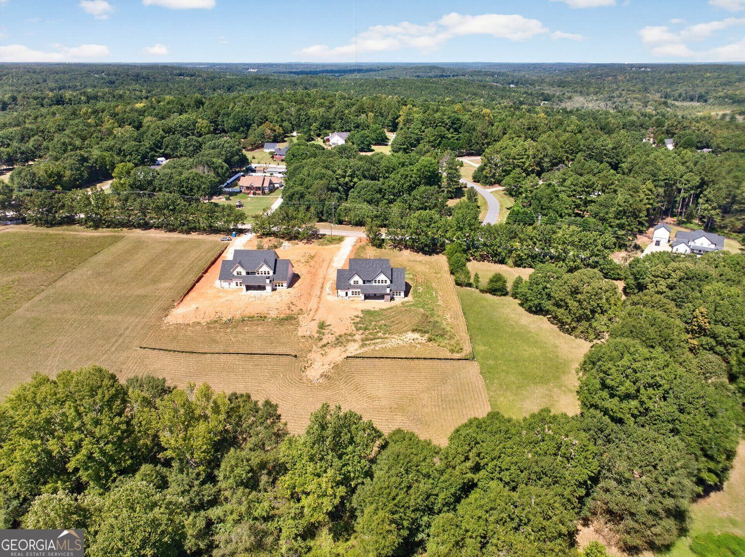Aerial view of two houses on cleared lots amid wooded countryside.