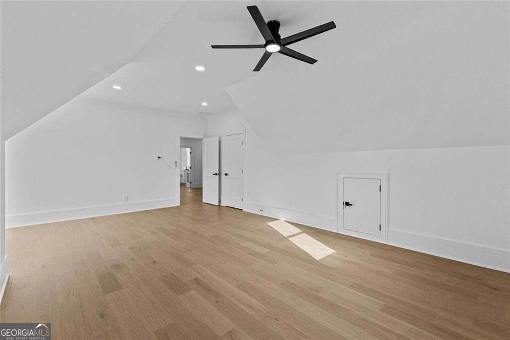 Finished upper-level room with sloped ceilings, light wood flooring, and a black ceiling fan.