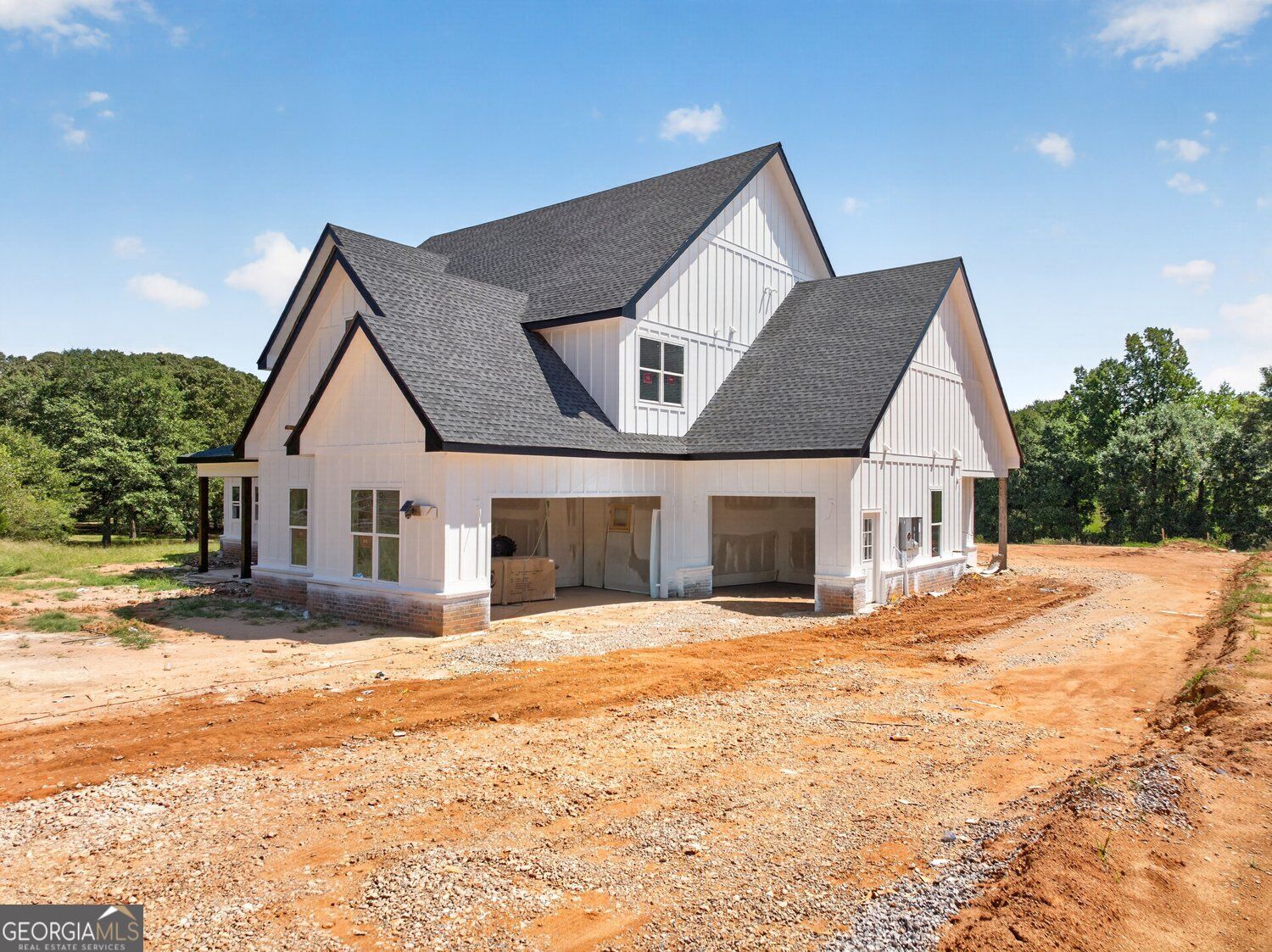 White multi-gabled house under construction with open garage bays and red dirt around it.