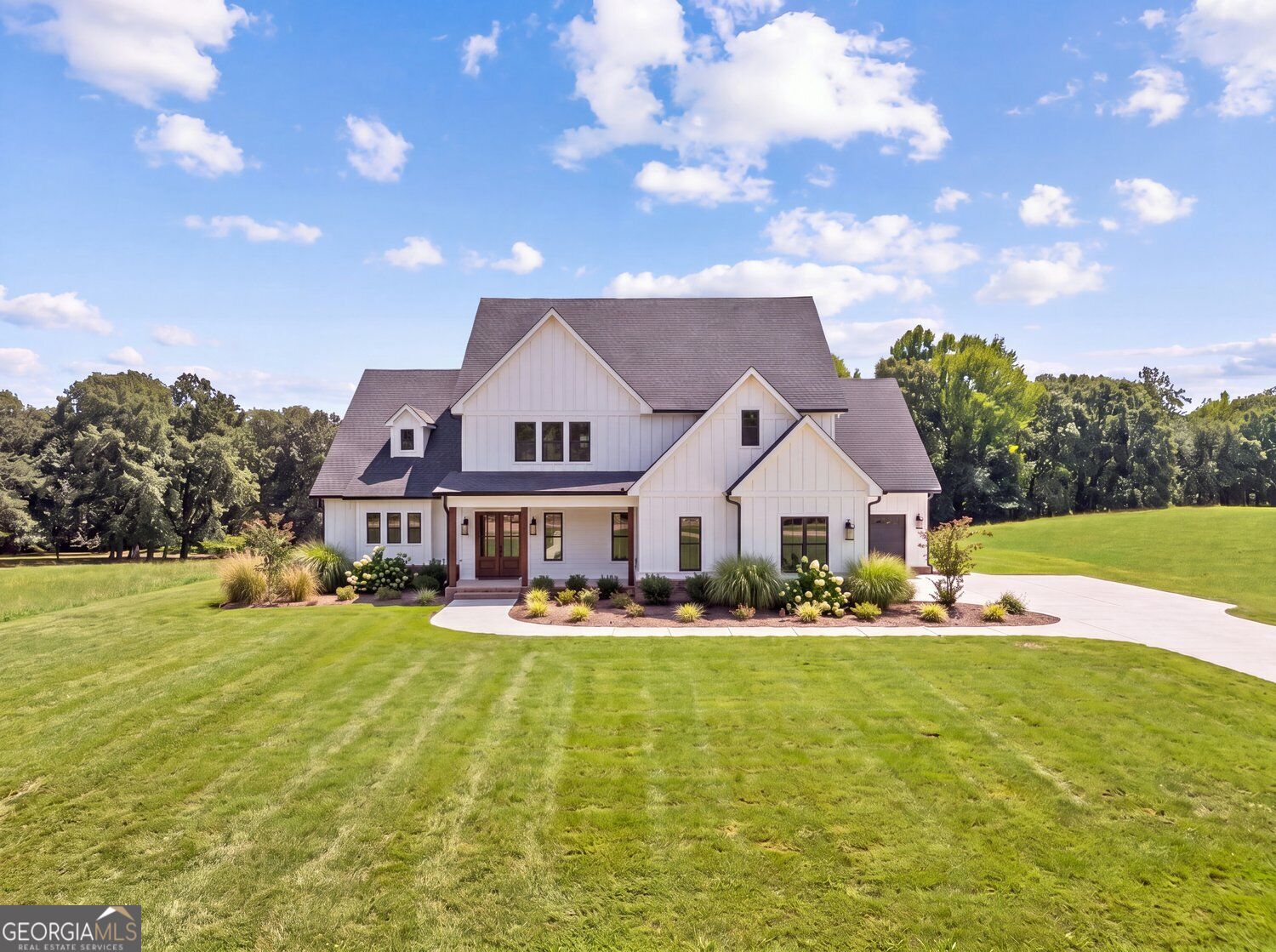 White farmhouse with multiple gables, landscaped beds, and a broad green lawn.