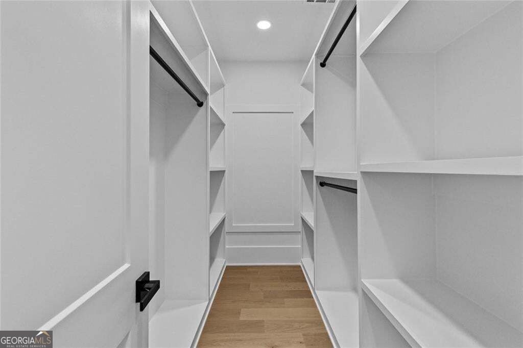 Walk-in closet with white built-in shelving, black hanging rods, and a light wood floor.