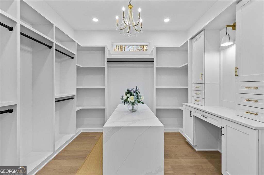 Walk-in closet with white built-ins, a central island, wood floors, and a chandelier.