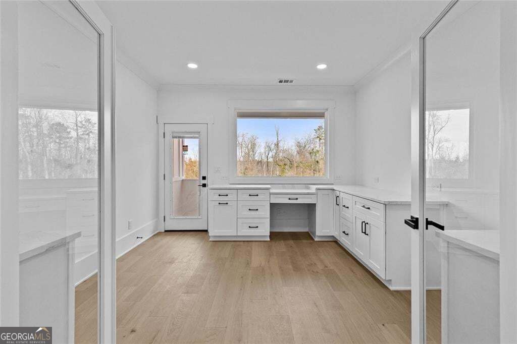 Empty room with white built-in desk cabinetry, light wood floors, and a large window.