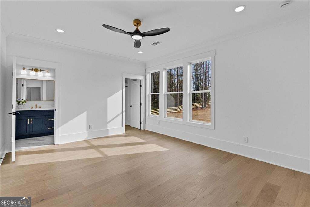 Vacant bedroom with a ceiling fan, three large windows, and an adjoining bathroom with a dark blue vanity.