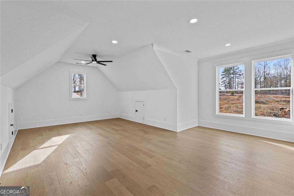 Empty upper-level room with sloped ceilings, light wood floors, and windows overlooking a field.