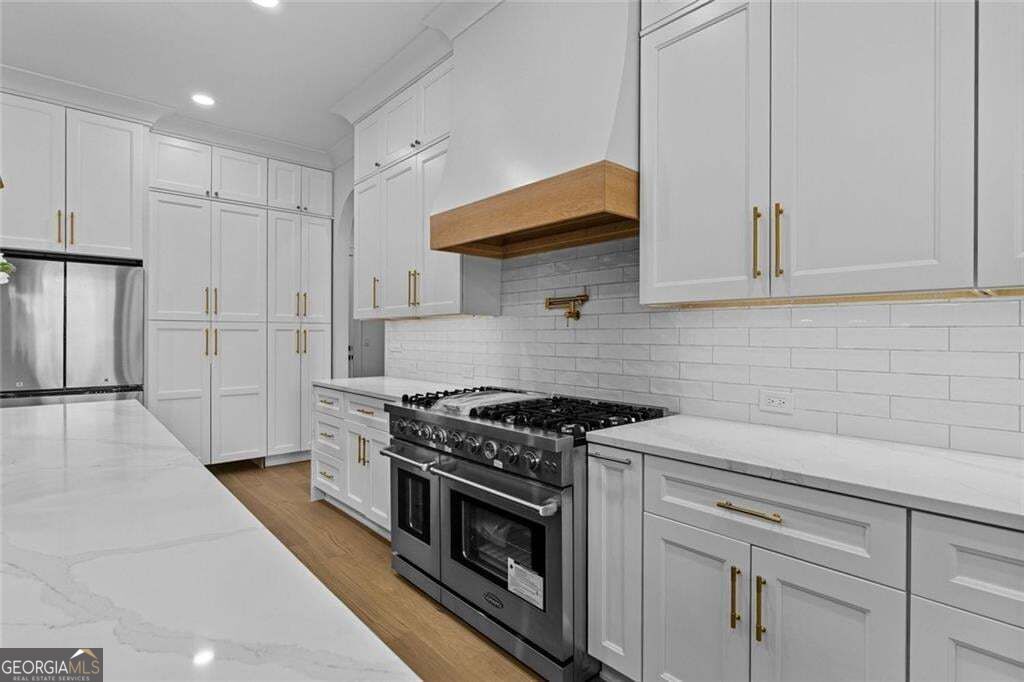 Kitchen with white cabinetry, stone counters, and a stainless-steel range beneath a wood-trimmed hood.
