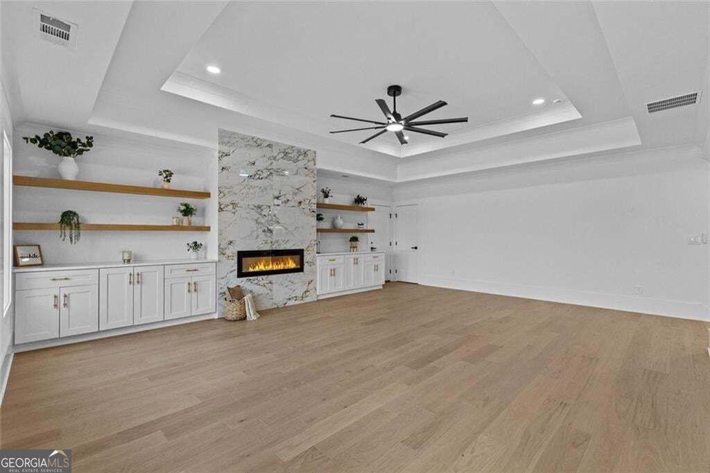 Living room with a marble fireplace, white built-ins, light wood floors, and a tray ceiling.