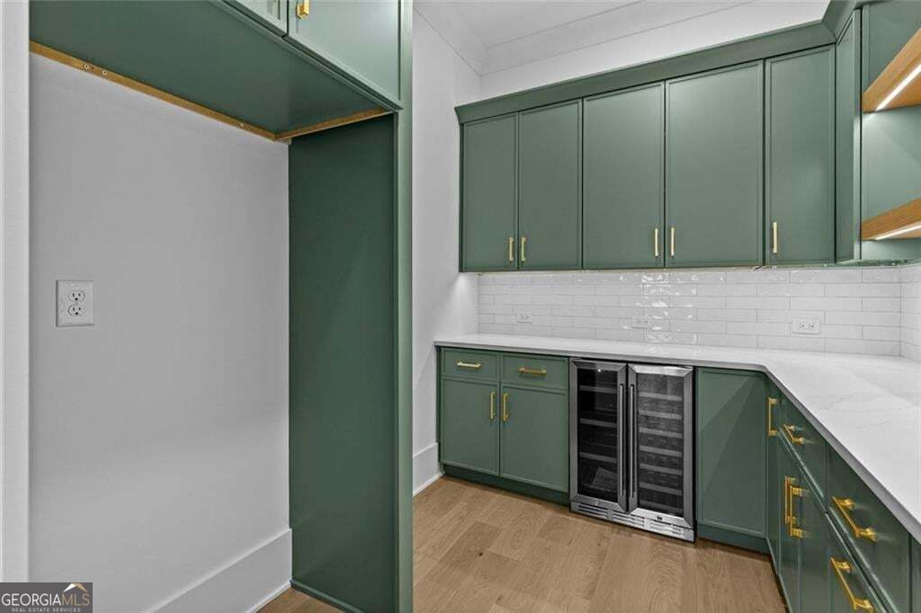 Wet bar with dark green cabinetry, white counters, and two glass-front beverage refrigerators.