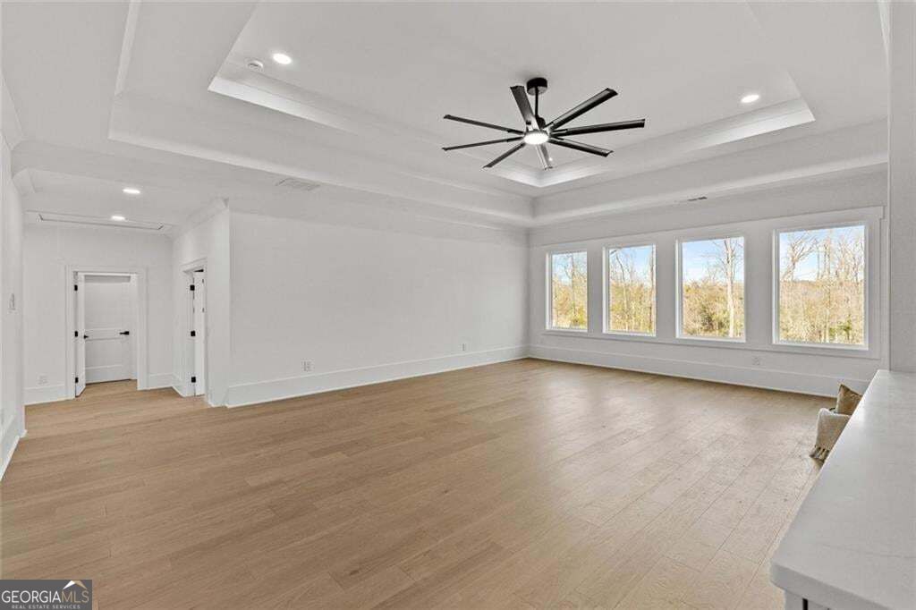 Spacious living room with light wood floors, a tray ceiling, modern fan, and four large windows.