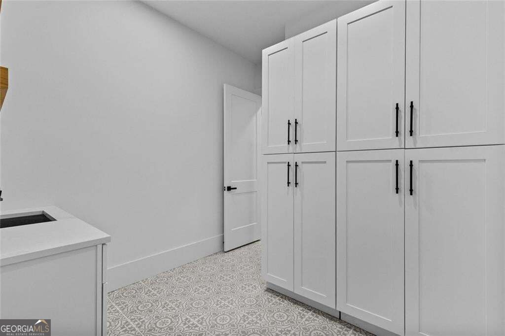 Laundry room with tall white cabinets, a countertop sink, and patterned gray tile floor.
