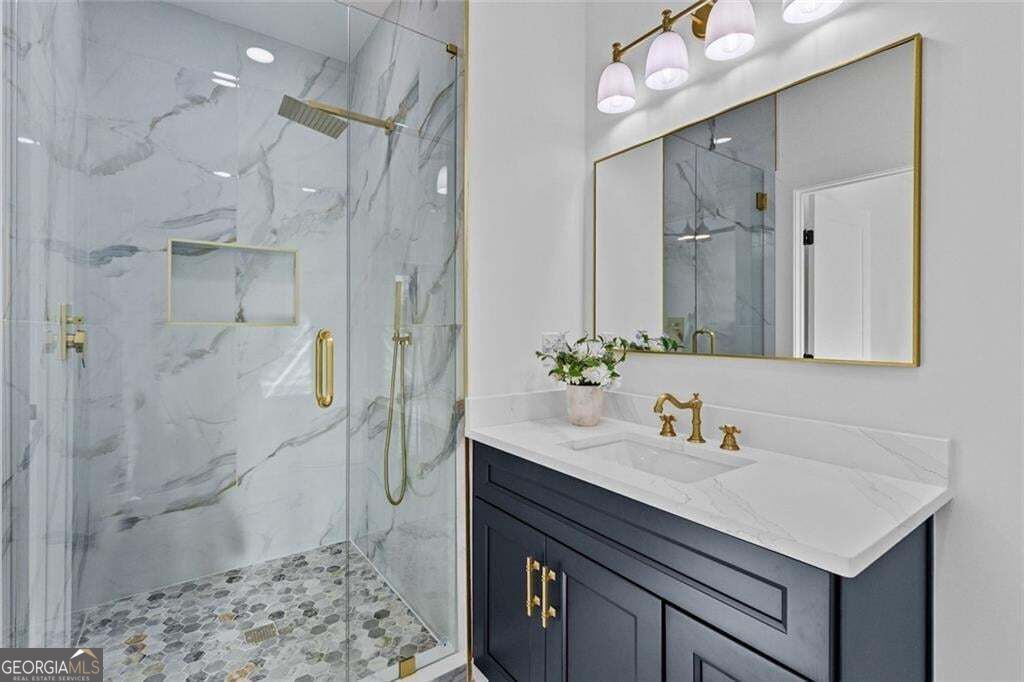Bathroom with a marble-look walk-in shower, pebble tile floor, and navy vanity with gold fixtures.