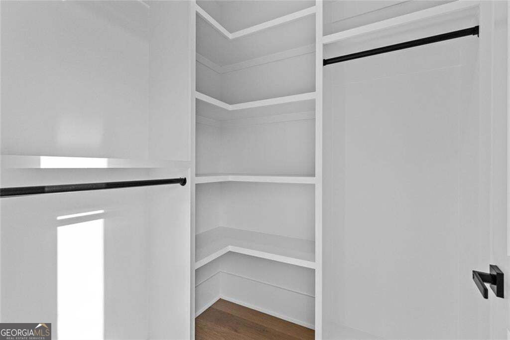 Walk-in closet with built-in corner shelves, hanging rods, and wood flooring.