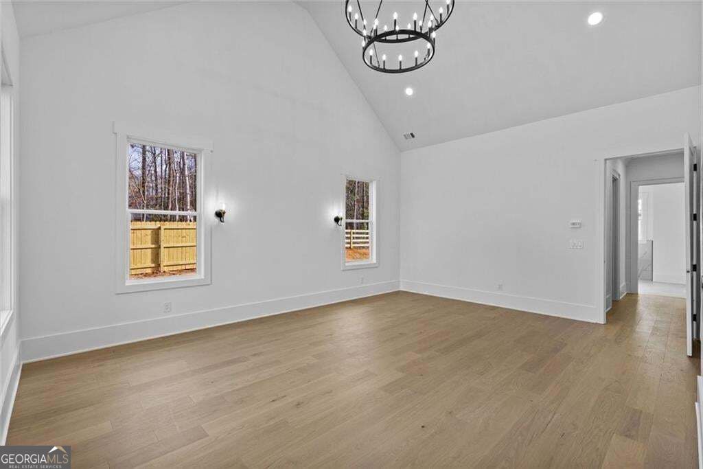 Vacant living room with light wood floors, vaulted ceiling, and windows overlooking a fenced yard.