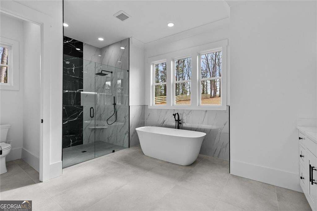 Modern bathroom with a freestanding tub, glass walk-in shower, and three windows overlooking trees.