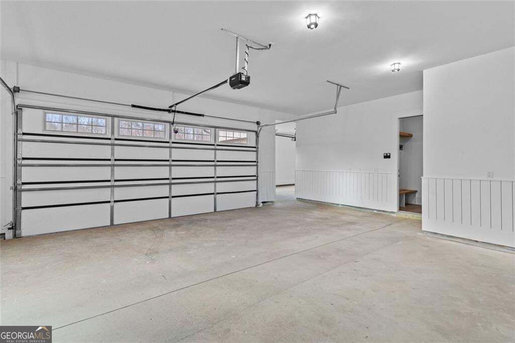 Empty garage with a wide overhead door, upper windows, and a concrete floor.