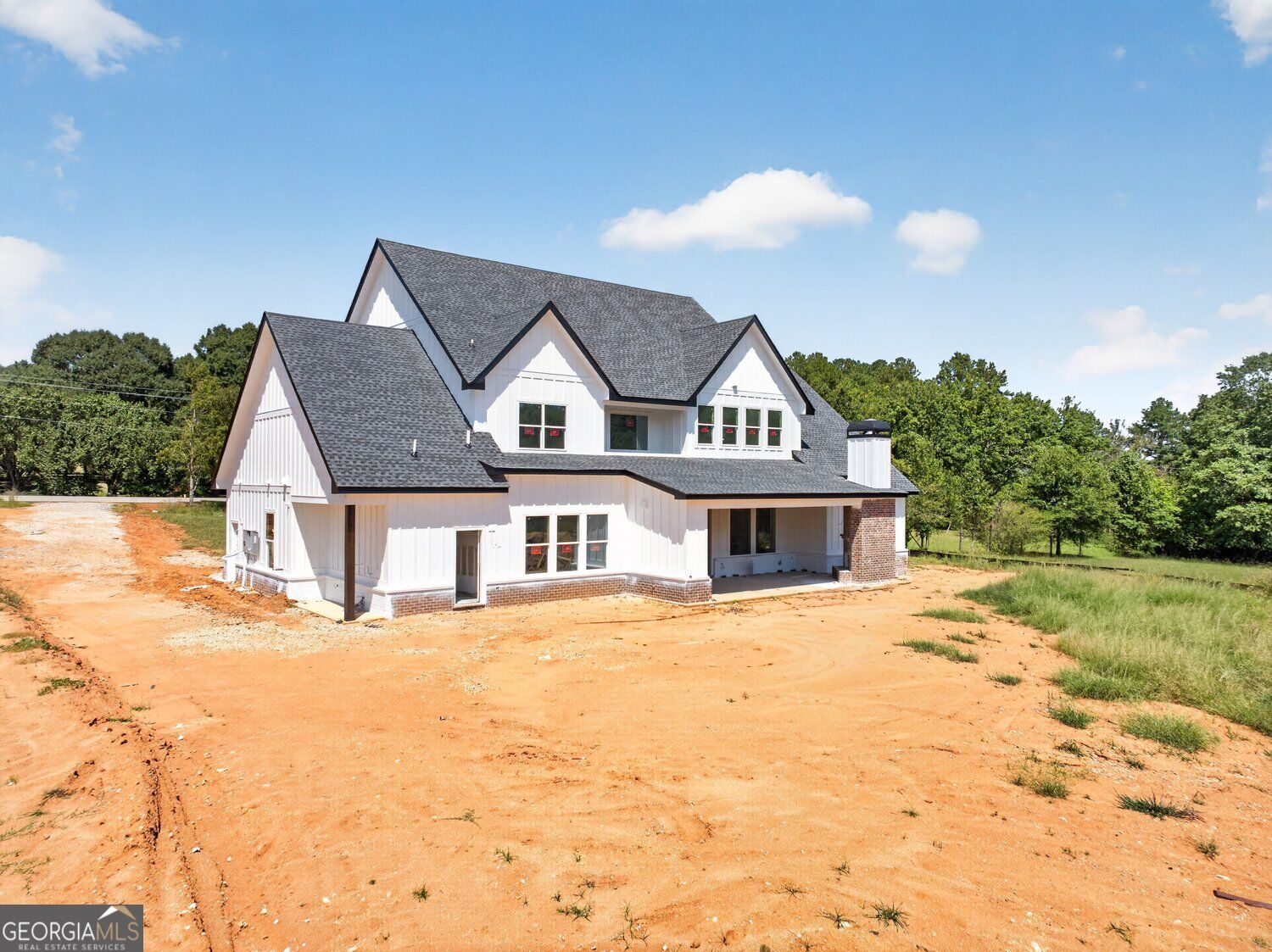 White two-story house with steep gables on a bare red-clay lot.