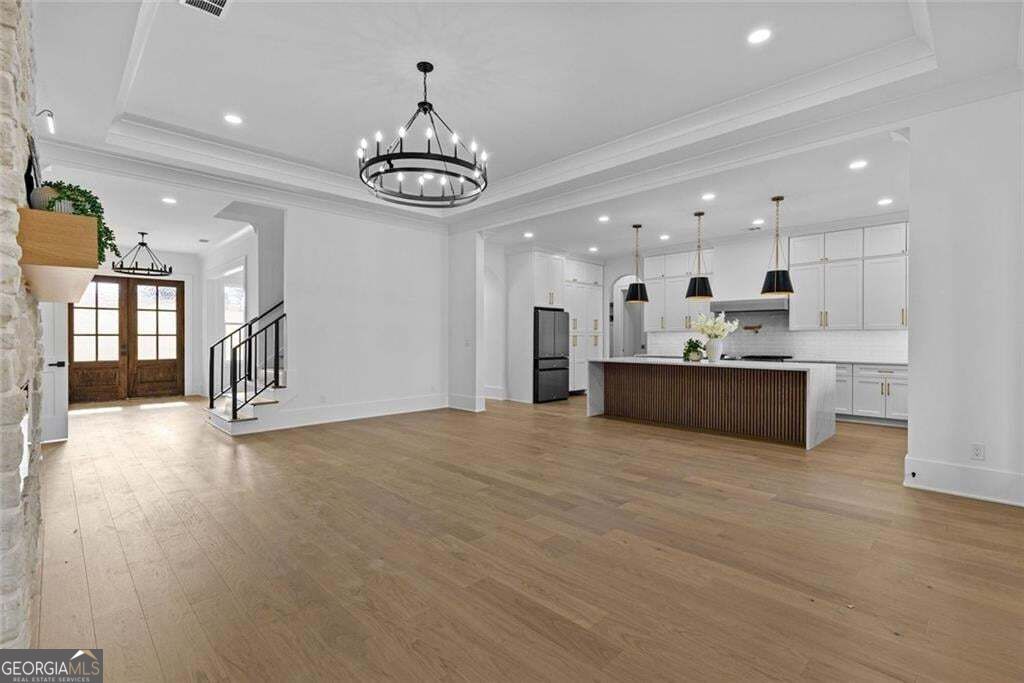 Open living area and white kitchen with a dark island, light wood floors, and double front doors.