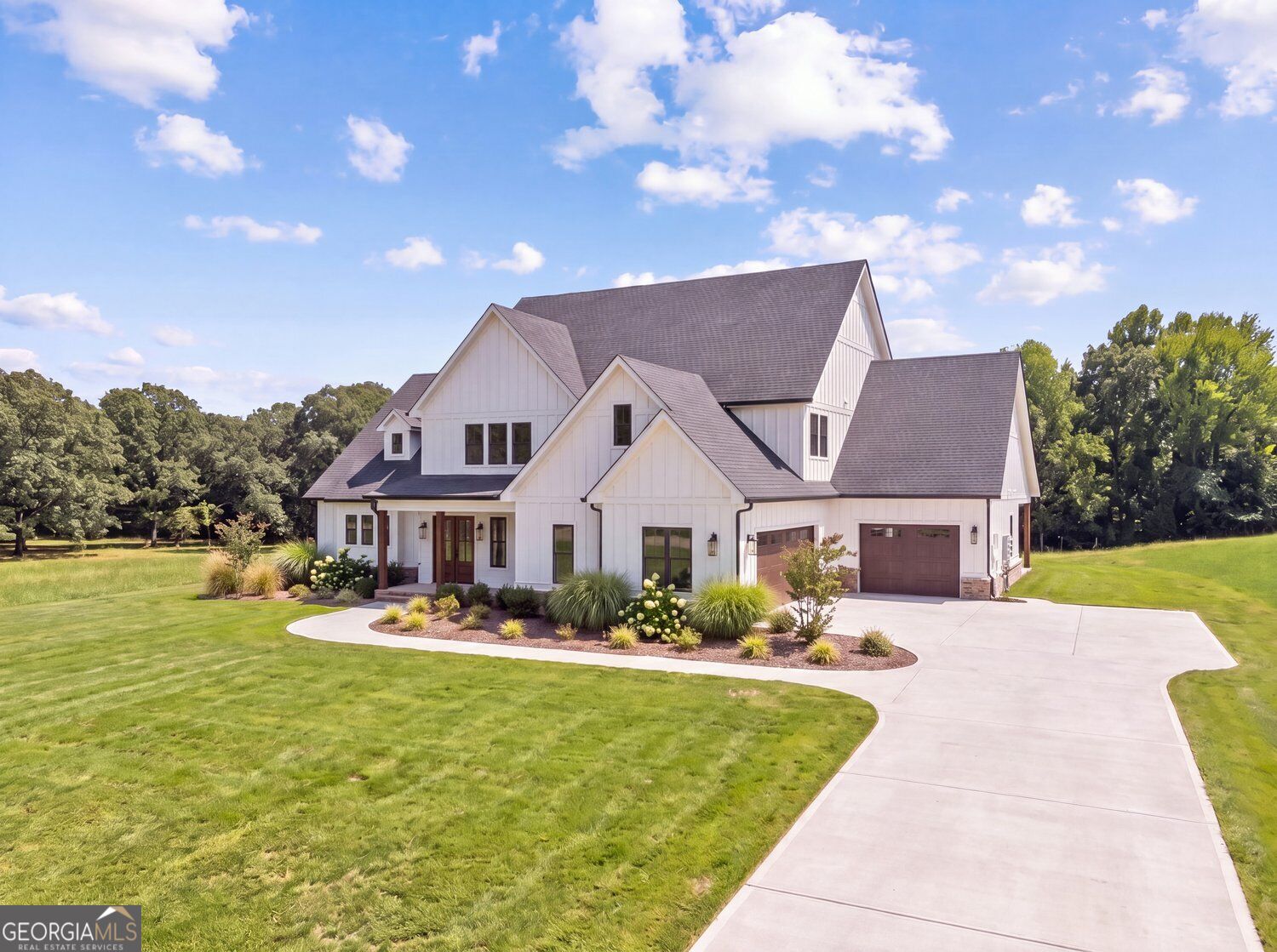White two-story home with multiple gables, a two-car garage, landscaped beds, and a curved driveway.