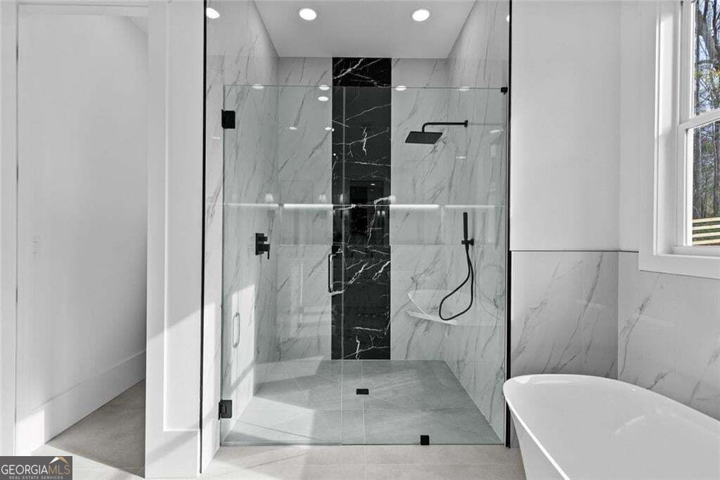 Modern bathroom with a glass walk-in shower, marble walls, black fixtures, and a freestanding tub.