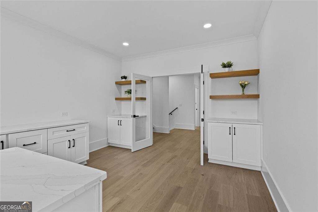 White kitchen with shaker cabinets, wood shelves, and a glass-paneled door opening to a hallway.