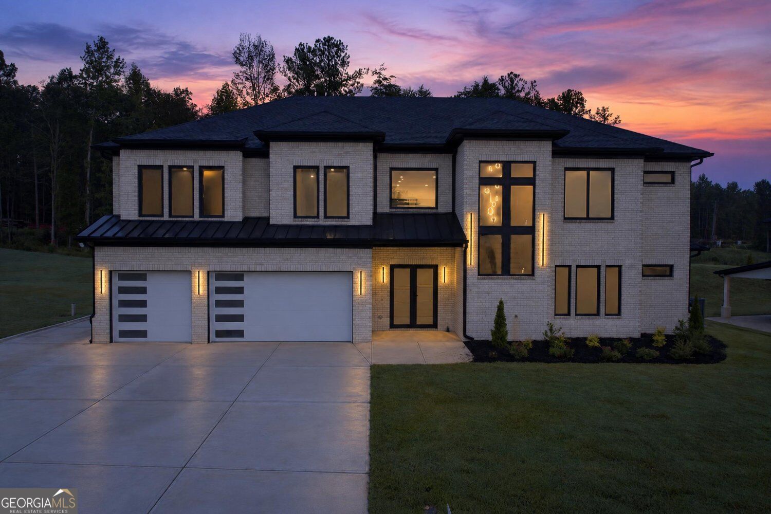 Two-story white brick home with a wide driveway and illuminated entry beneath a pink-purple dusk sky.