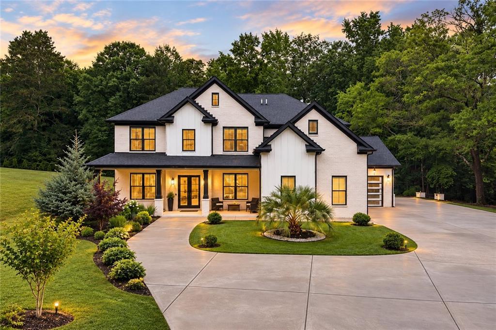 Two-story white house with dark gabled roofs, landscaped lawn, and curved driveway at dusk.