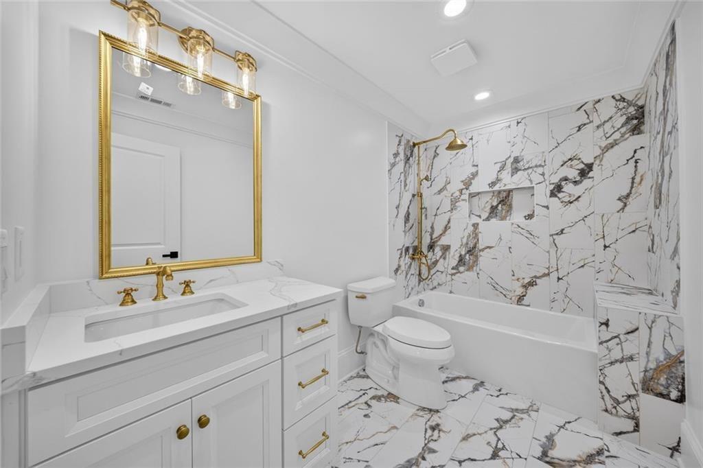 Bathroom with a white vanity, gold fixtures, and a marble-look tiled tub surround.