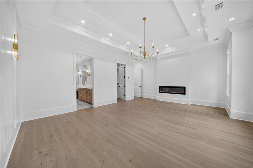 Unfurnished living room with a tray ceiling, brass chandelier, and built-in linear fireplace.