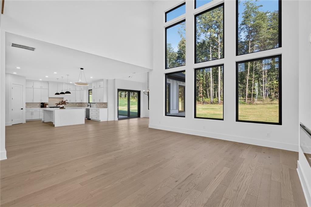 Open living room and kitchen with tall windows overlooking trees and a lawn.