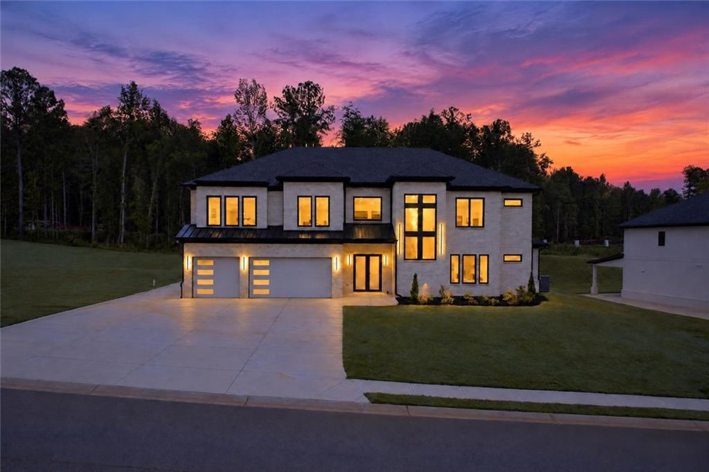 Two-story home with illuminated windows and a broad driveway beneath a vivid sunset.