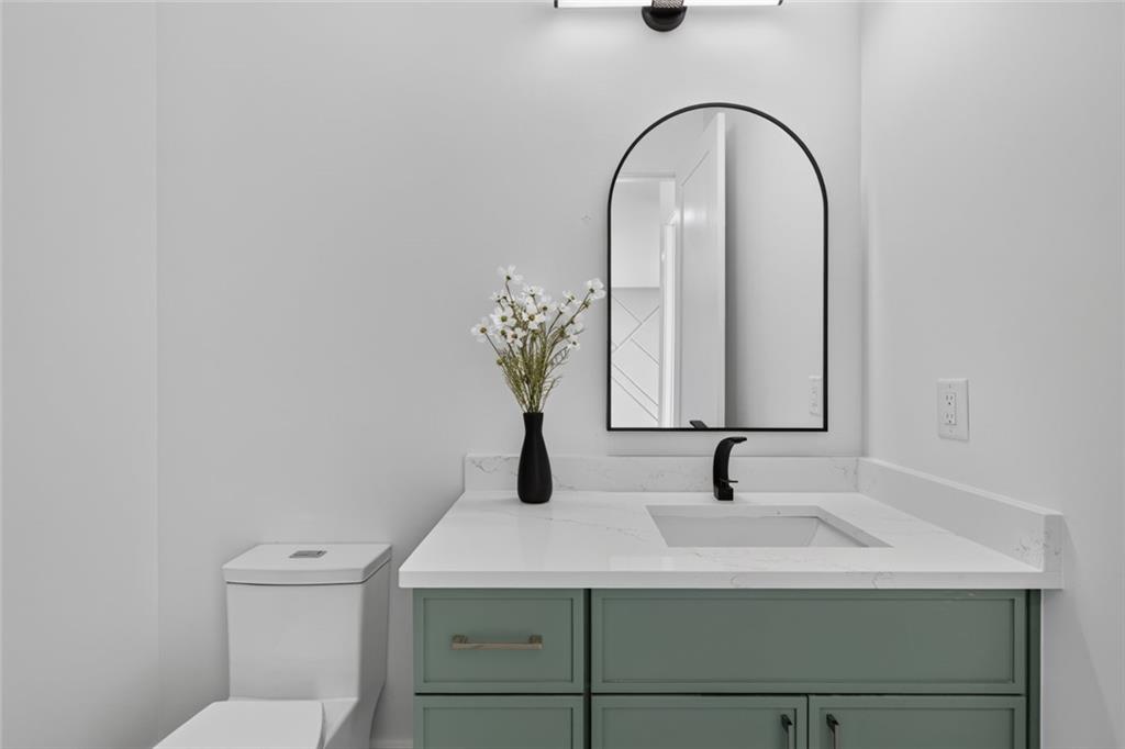 Bathroom vanity with sage-green cabinetry, a white countertop, black faucet, and arched mirror.