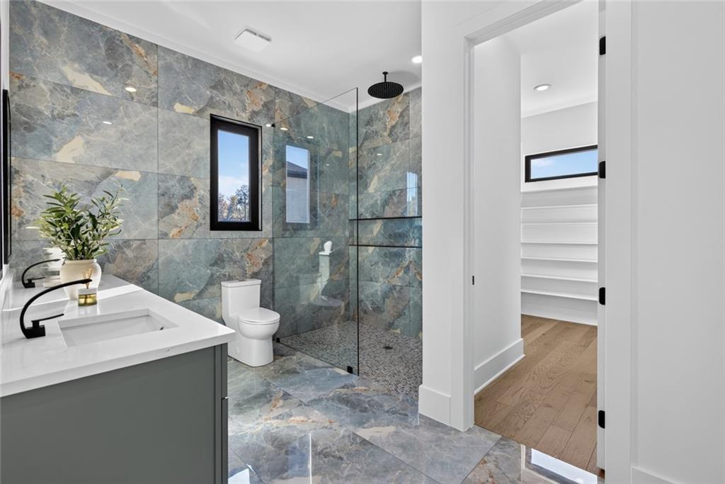 Modern bathroom with a glass walk-in shower, marble-patterned tile, and gray double-sink vanity.