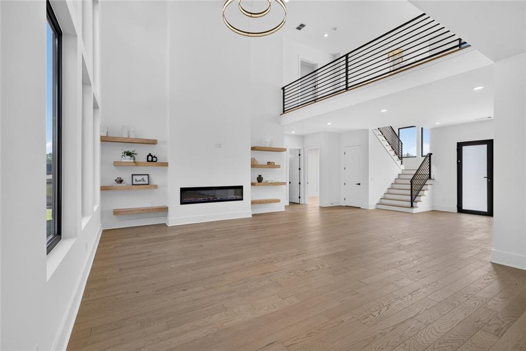 Double-height living room with wood floors, a linear fireplace, floating shelves and an open staircase.
