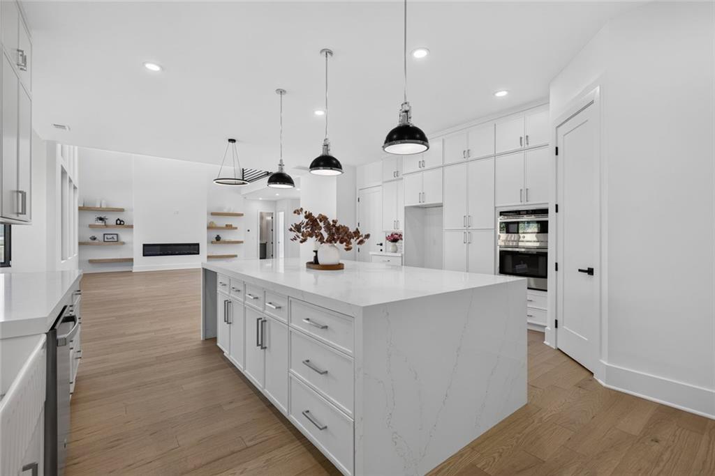 Modern white kitchen with a large island, pendant lights, and light wood floors.