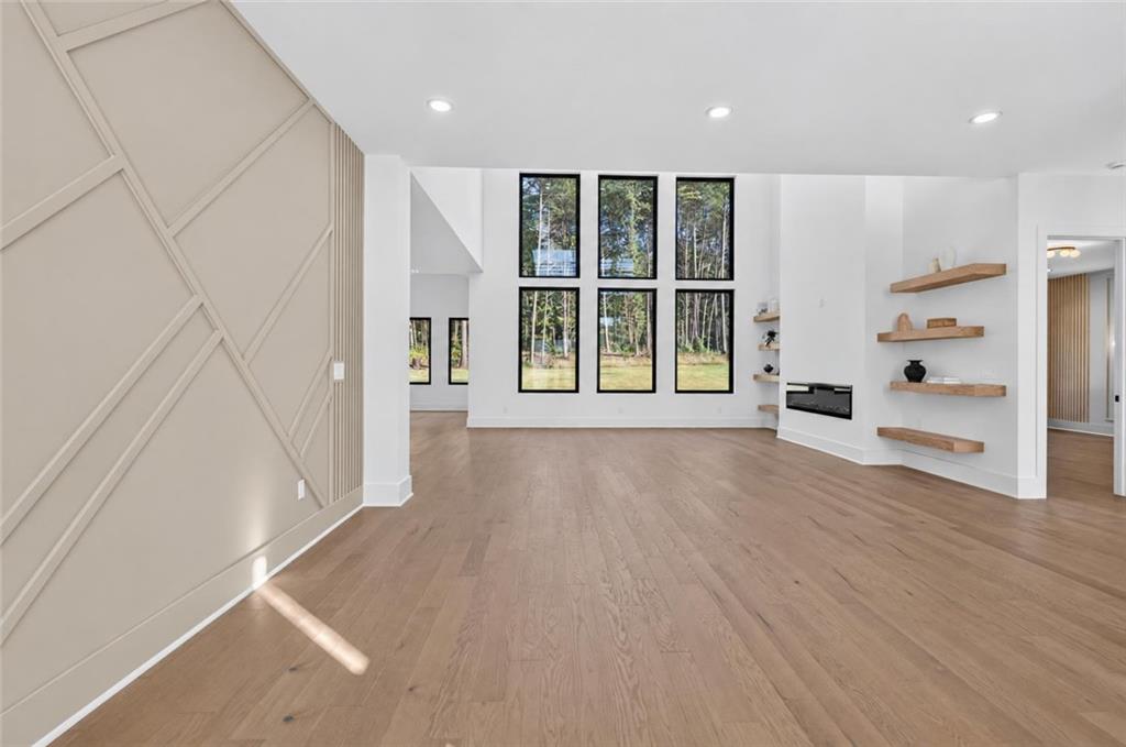 Unfurnished living room with tall windows, a geometric accent wall, and floating shelves beside a fireplace.