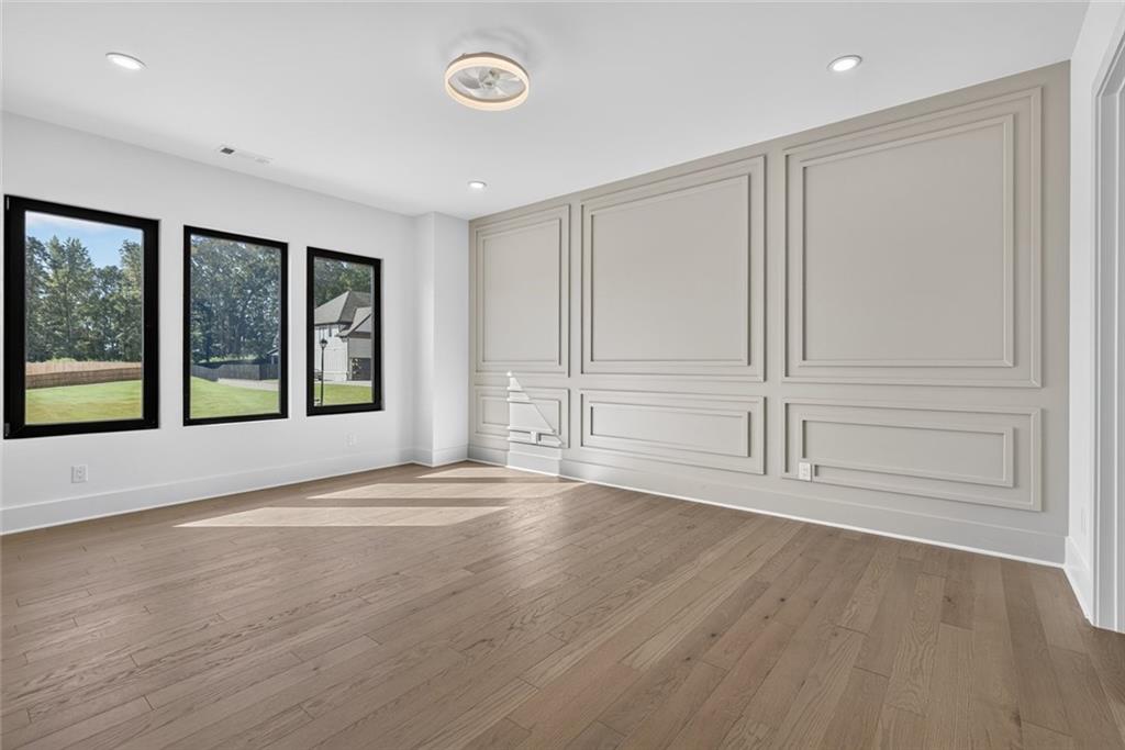 Empty room with a white paneled accent wall, wood floors, and three black-framed windows.